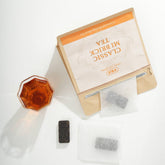 Box of tea bags with a glass of tea on a white background