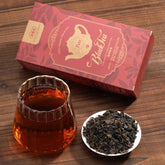 Tea packaging, glass of tea, and bowl of tea leaves on a wooden surface
