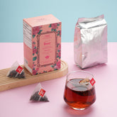 Tea packaging including a box, bag, and glass of tea on a pink surface with a light blue background.