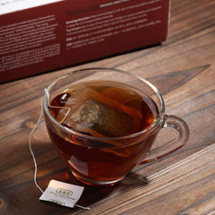 Clear glass cup of tea with a tea bag on a wooden surface, next to a box of tea.
