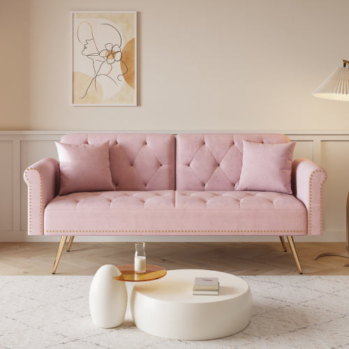 A 69.7-inch-long sofa bed covered in pink velvet fabric, featuring nail head trim and accompanied by a matching throw pillow