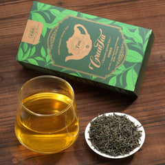 Tea packaging, glass of tea, and tea leaves on a wooden surface