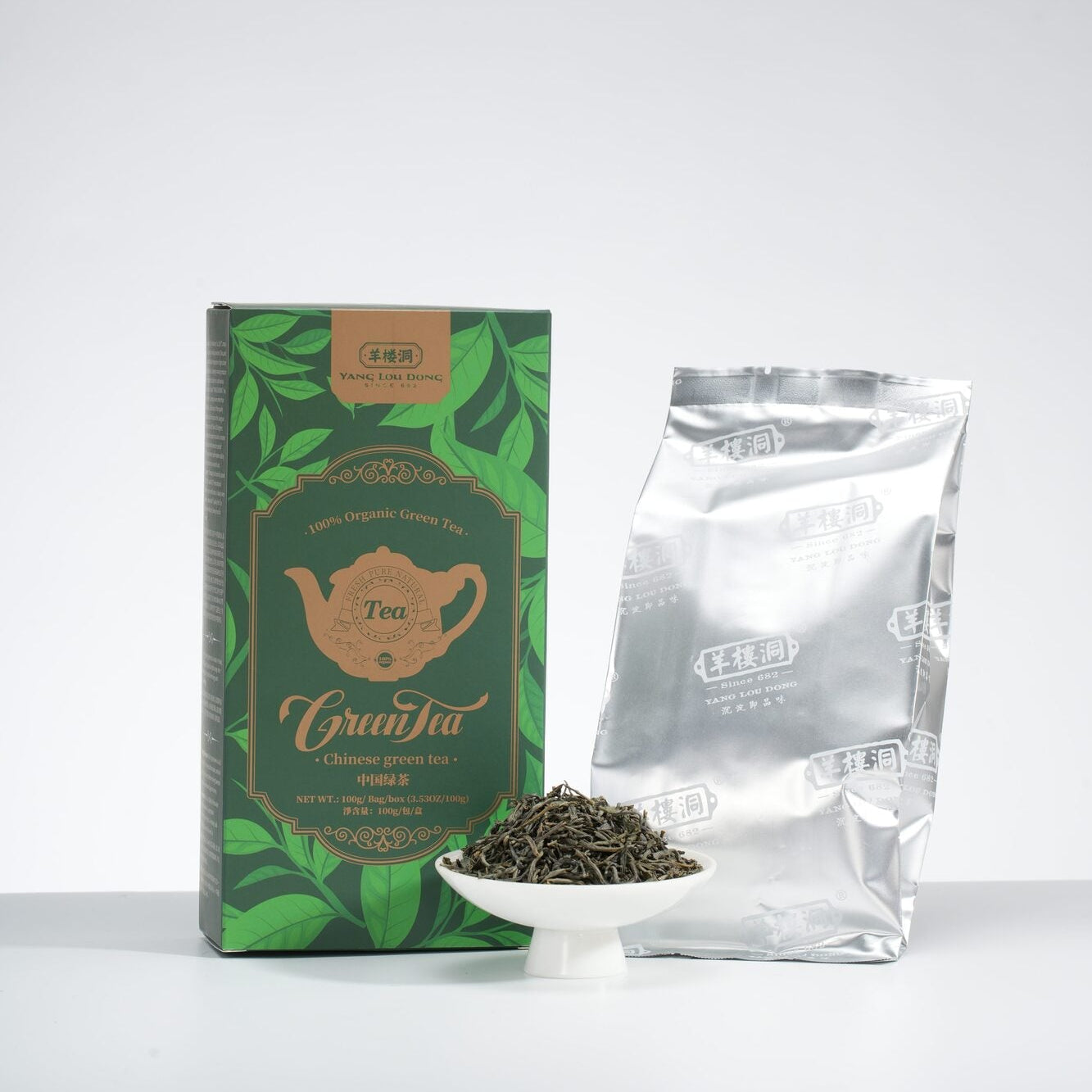 Tea packaging including a green box, silver bag, and a small bowl of tea leaves on a white background