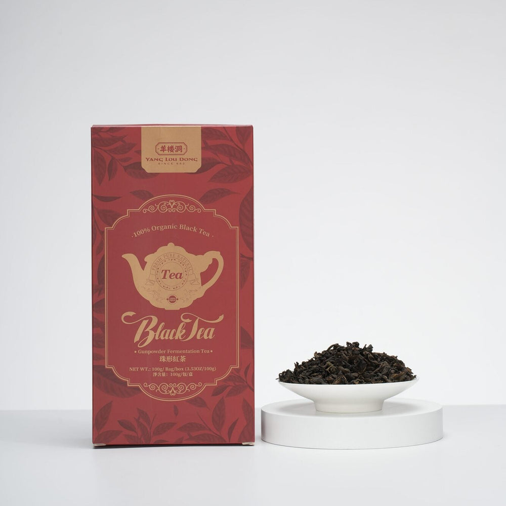 Red tea box labeled 'Black Tea' with a small bowl of black tea leaves on a white background