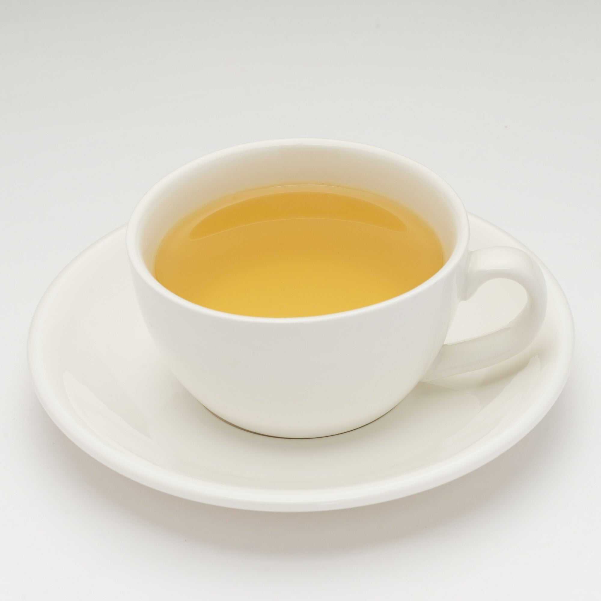 White cup and saucer with yellow liquid on a white background
