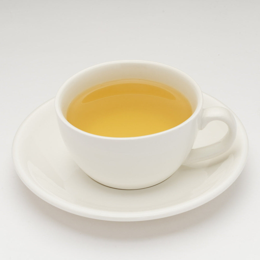 White cup and saucer with yellow liquid on a white background